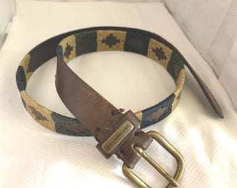 May include: A brown leather belt with a woven pattern in shades of beige, green, and blue. The belt buckle is brass and has the text "KEVYN'S VON" engraved on it.
