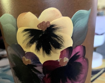 May include: A brown metal container with a painted design of three purple, yellow, and burgundy pansies with black centers. The container has the word "Verdick" written on the bottom.