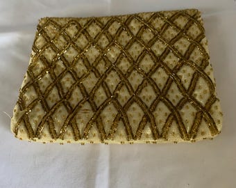 May include: A cream-coloured rectangular clutch bag featuring a gold beaded lattice design. The gold beads form a textured, geometric pattern across the surface, providing an elegant finish to the accessory.