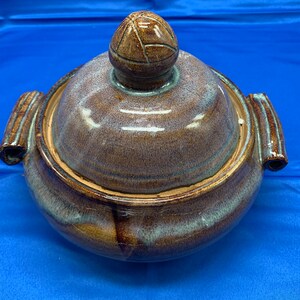 May include: A brown ceramic serving dish with a lid. The dish has a blue and brown glaze with a swirl pattern. The lid has a rounded knob on top.