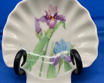 May include: A white porcelain seashell dish with a raised edge, featuring a painted design of two purple and blue iris flowers with green leaves.