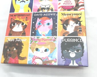 May include: A square puzzle box with nine illustrated cat portraits, each styled after a famous musician. The box includes the text "500 PIECE PUZZLE" and the brand name "mudpuppy". The cat portraits include Freddie Purrcury and David Meowie.
