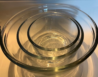 May include: Three clear glass mixing bowls of different sizes, nested inside each other.
