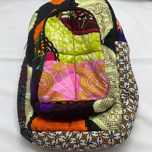 May include: A quilted backpack featuring a patchwork design of various vibrant fabrics. The exterior displays a mix of patterns including lime green, bright pink, orange, black, and white geometric and floral motifs with a zippered front pocket.
