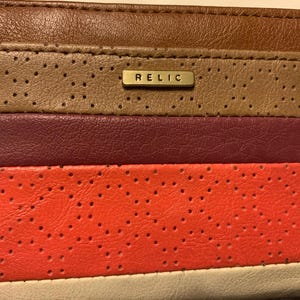 May include: A multi-colored leather card holder with a perforated design. The card holder features horizontal stripes in brown, tan, burgundy, orange, and white. A small gold-colored metal plate with the word "RELIC" is centered on the top.