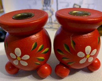A pair of small wooden candlestick holders in a red folk art design.