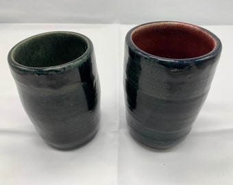 May include: Two ceramic mugs with a dark blue glaze. One mug has a green interior and the other has a reddish brown interior.