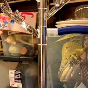 May include: A clear acrylic jewelry stand shaped like a tree with multiple branches. The stand is made of a shiny, chrome-like material.