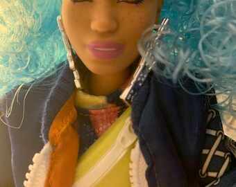 A bendy and curvy standing 12 inch doll with blue curly hair.