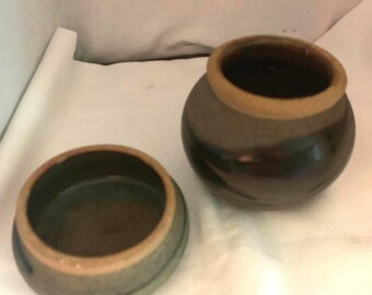 May include: Two brown ceramic pots with a glazed finish. The larger pot has a wider opening and a slightly rounded shape. The smaller pot has a smaller opening and a more rounded shape. Both pots have a brown and blue glaze with a light brown rim.