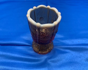 May include: A vintage glass candy dish with a footed base. The dish is made of iridescent glass with a cranberry red color and a white opalescent rim. The dish has a floral design.