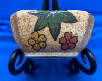 A small ceramic pottery bowl in a flowered glaze on brown.