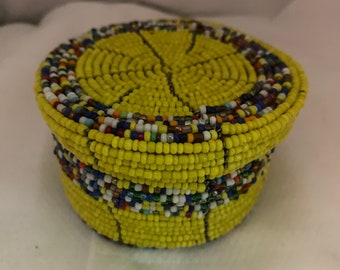 May include: A small, round, yellow beaded box with colorful accents. The box is made of tiny beads woven together in a circular pattern.