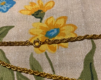 May include: A gold rope chain necklace with a lobster clasp fastening. The chain is lying on a floral fabric background.