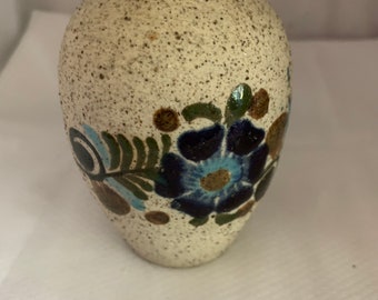 May include: A small, white ceramic vase with a speckled texture and a floral design in shades of blue, green, and brown.