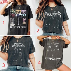 Puede incluir: Una colección de cuatro camisetas gris carbón con gráficos de Twenty One Pilots. Cada camiseta muestra imágenes de la banda, texto estilizado y firmas en tinta blanca o negra, exhibiendo varios diseños artísticos.