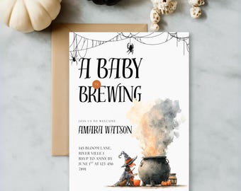 May include: A white invitation card with the text "A Baby is Brewing" in black. The card features a watercolor illustration of a witch, cauldron, and smoke. Decorative pumpkins and skulls are in the background.