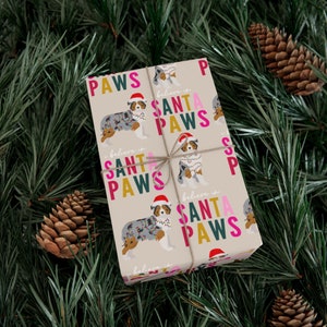 Op de afbeelding: Beige inpakpapier met een herhalend patroon van Australian Shepherd honden die kerstverlichting dragen en de tekst "Geloof in Sinterklaas Pootjes".