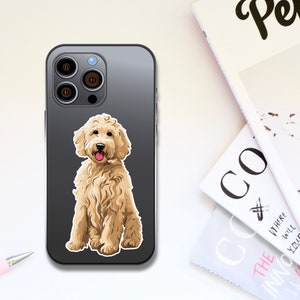 Puede incluir: Una funda de iPhone negra con una pegatina blanca de un perro caniche dorado sentado encima. El perro tiene la nariz rosa y sonr&iacute;e.