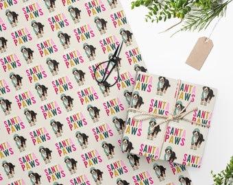 May include: Wrapping paper featuring a repeating pattern of a dog dressed as Santa Claus with the text "SANTA PAWS" in colorful letters. A wrapped gift and scissors are also visible.