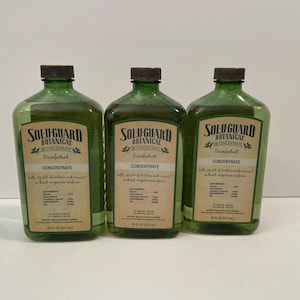Könnte beinhalten: Drei identische grüne Glasflaschen mit Solu-Guard Botanical 2X Concentrate Desinfektionsmittel. Jede Flasche hat ein beiges Etikett mit schwarzer Schrift, einen dunkelbraunen Schraubverschluss und ein Volumen von 473 ml auf dem Etikett.