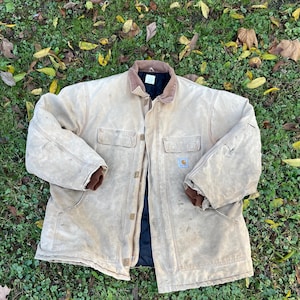 May include: A tan work jacket with a brown corduroy collar and brown cuffs. The jacket has four front pockets and a black lining. A small logo patch is visible on one of the pockets.