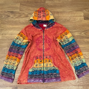 Può includere: Una felpa con zip e cappuccio color rosso slavato, caratterizzata da maniche e cappuccio decorati con fasce orizzontali di tessuto arcobaleno, ciascuna stampata con un motivo ripetitivo di impronte di zampe nere. Include due tasche frontali.