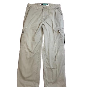 May include: Khaki cargo trousers with multiple pockets and a relaxed fit. The trousers feature a button and zip closure, belt loops, and a small tag near the waistband. The trousers are made of a durable fabric.