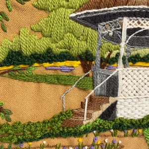 May include: Embroidered landscape scene showing a gazebo with a brown roof, grey supports, and white lattice. The scene includes green trees, a small pond, and a path with flowers. The embroidery is on a tan fabric.