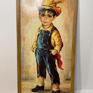 Könnte beinhalten: Ein gerahmtes Gemälde eines jungen Jungen, der einen gelben Hut mit einer Feder, ein gelbes Hemd, eine blaue Latzhose und ein rotes Bandana trägt. Der Junge hat braunes Haar, blaue Augen und Sommersprossen. Das Gemälde ist mit "Madisone" signiert.