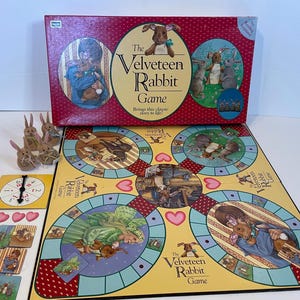 Puede incluir: Un juego de mesa basado en la clásica historia infantil, El Conejo de Terciopelo. El tablero de juego presenta ilustraciones del conejo y otros personajes de la historia. La caja presenta un fondo rojo con el título del juego en letras doradas.