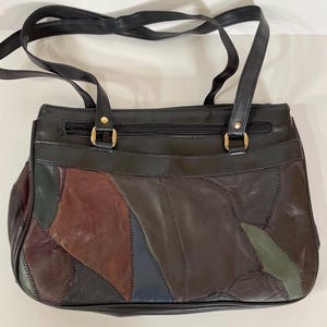 May include: A black leather handbag with a patchwork design in shades of brown, green, and blue. The bag has two handles and a zipper closure. The hardware is gold-colored.