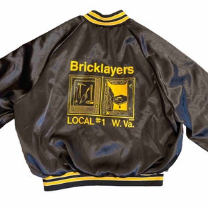 May include: Black satin bomber jacket with yellow and white striped trim. The back of the jacket features a yellow embroidered design with the text "Bricklayers Local #1 W. Va."