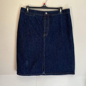 May include: A dark blue denim skirt with a front split, hanging on a black hanger. The skirt features a button closure and visible stitching. A classic style skirt, suitable for various outfits.