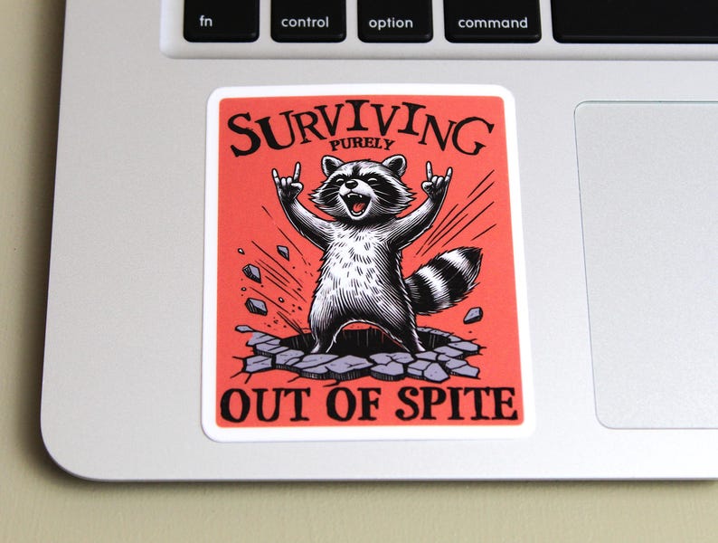 K&ouml;nnte beinhalten: Ein rechteckiger Aufkleber mit rotem Hintergrund und einer Waschb&auml;r-Illustration. Der Waschb&auml;r bricht durch eine Oberfl&auml;che, die Arme in einer Rock'n'Roll-Geste erhoben. Der Text "SURVIVING PURELY OUT OF SPITE" ist in Schwarz gedruckt.