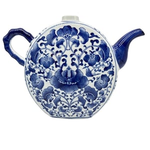 May include: A white ceramic teapot with a blue and white floral design. The teapot has a round body and a spout on the side. The handle is attached to the side of the teapot.