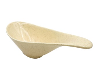 May include: A speckled beige ceramic serving dish with a long, curved handle. The dish is designed to hold sauces or dips.