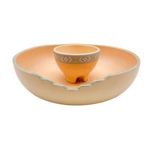 May include: A ceramic serving bowl with a smaller bowl in the center. The larger bowl is light beige with a light blue rim. The smaller bowl is light orange with a geometric pattern in blue, yellow, and purple.