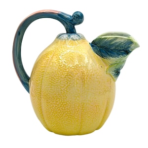 May include: A yellow ceramic pitcher shaped like a lemon with a blue handle and green leaf spout.