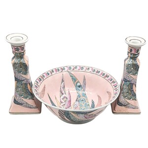 May include: A set of three pink and white ceramic pieces with a floral design. The set includes a bowl and two candle holders.