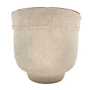 May include: A white ceramic planter with a rough, textured surface. The planter has a wide, rounded base and a slightly flared rim.