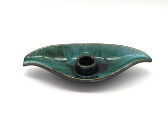 May include: A teal green ceramic candle holder shaped like a leaf with a single candle holder in the center.