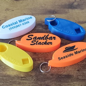 May include: Five oval-shaped keychains in white, blue, yellow, and orange. The white keychain has "Coastal Marine" and a phone number. The orange keychains have "Sandbar Slacker" and "Seaside Marina" printed on them. The blue and yellow keychains have "PlugKeyper" printed on them.