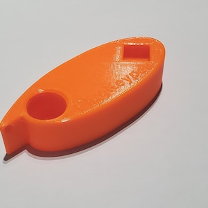Op de afbeelding: Een oranje sleutelorganizer met een afgeronde vorm, met een cirkelvormig gat en een vierkante opening. Het woord "keyp" is zichtbaar op het oppervlak. Het item is gemaakt van een solide materiaal en ligt op een wit oppervlak.