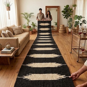 Puede incluir: Una alfombra larga, negra y beige con un patrón geométrico. La alfombra presenta rayas beige horizontales sobre un fondo negro. La alfombra está hecha de un material tejido y se exhibe en un salón.
