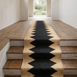 May include: A long, rectangular runner rug featuring a natural tan woven texture with a bold, central black zigzag pattern running the entire length. The runner is positioned to cover the center of a wooden staircase and floor.