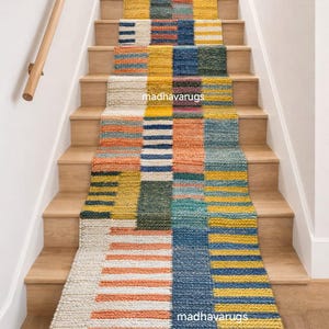 May include: A multi-coloured stair runner with a geometric design. The runner has a patchwork pattern with blocks of orange, yellow, blue, and green. The stair treads are made of light-coloured wood, and a wooden handrail is visible on the left.