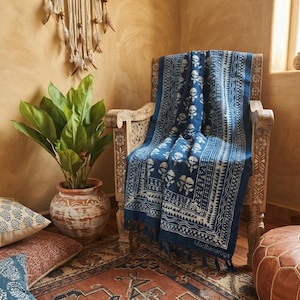 May include: A rectangular blue and white throw blanket featuring a repeating floral block print pattern and a decorative border with fringe edges. The fabric displays the text Madhavarugs printed in the lower right corner of the textile.