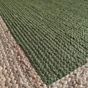 May include: A rectangular rug with a woven design. The rug features a central section of olive green, bordered by a natural tan color. The texture of the rug appears to be coarse and durable, suitable for high-traffic areas.