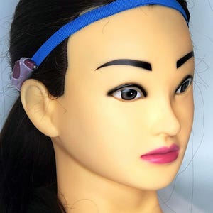May include: A blue headband with a purple and silver hearing aid attached to the left side.